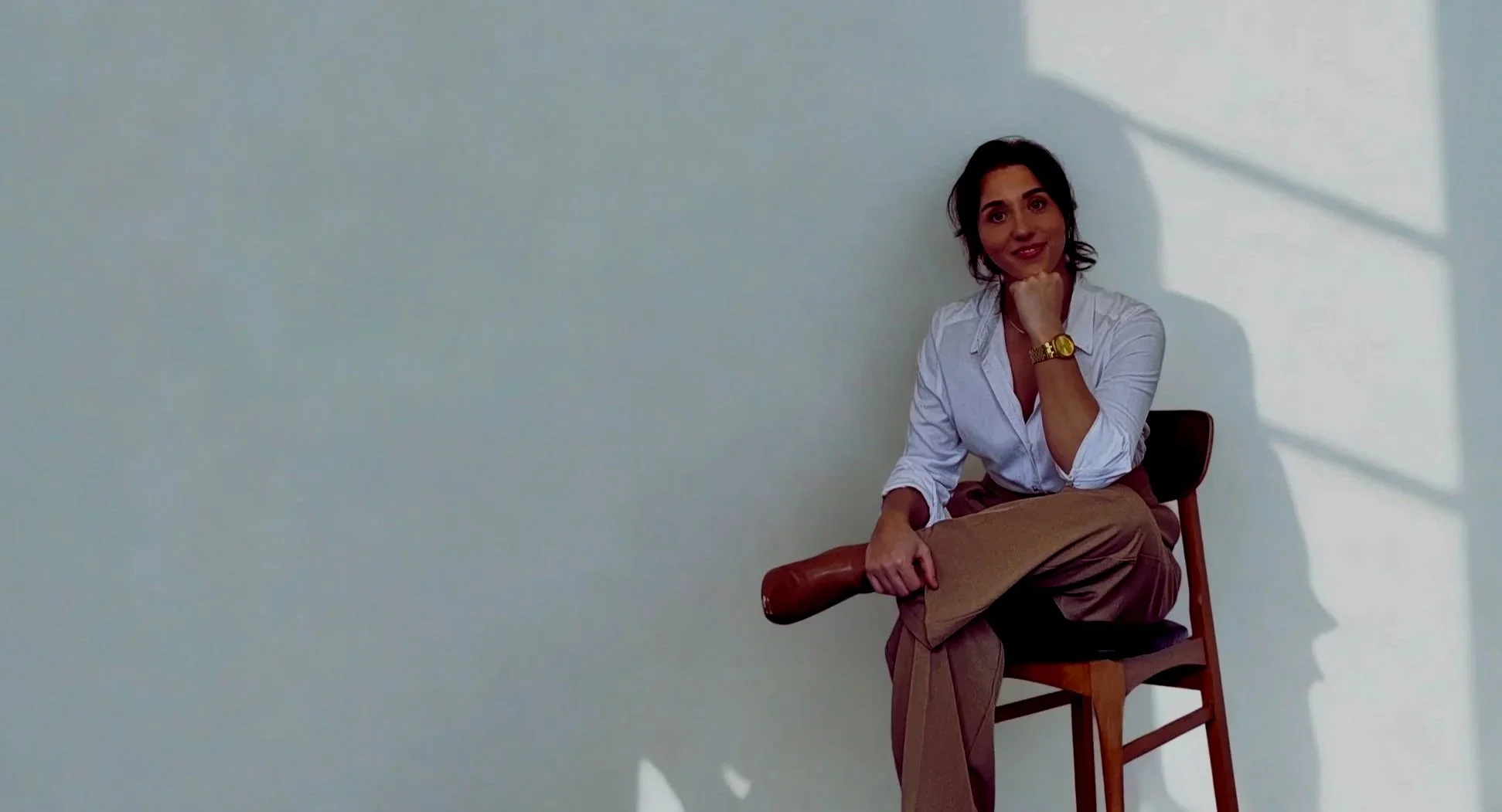 Rebecca Bromley sitting on a wooden chair against a sunlit wall